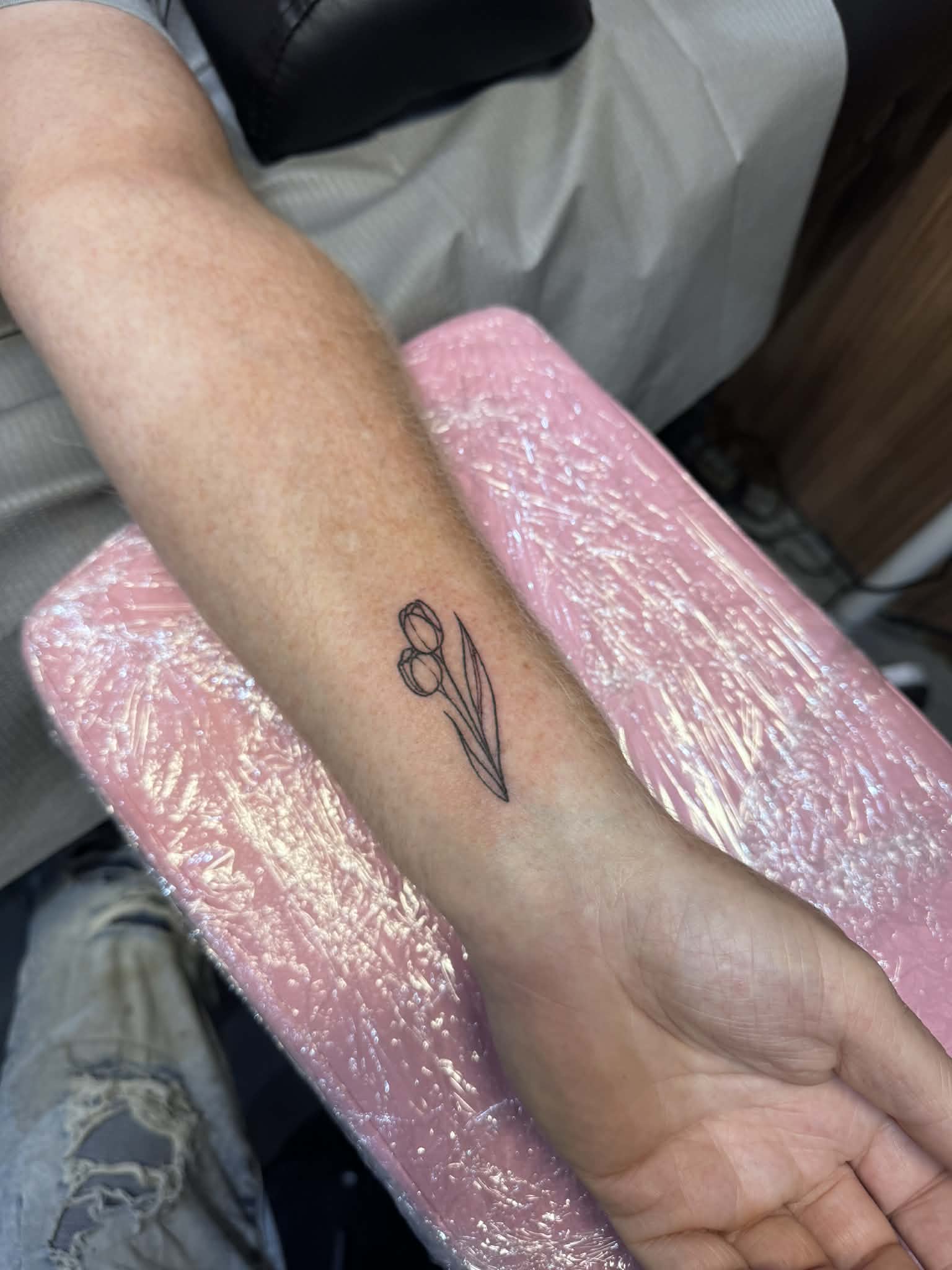 Fine line tulip tattoo on a forearm, demonstrating precise minimalist artistry by AJ at Poking Hazard Tattoo in Edmonton, AB.