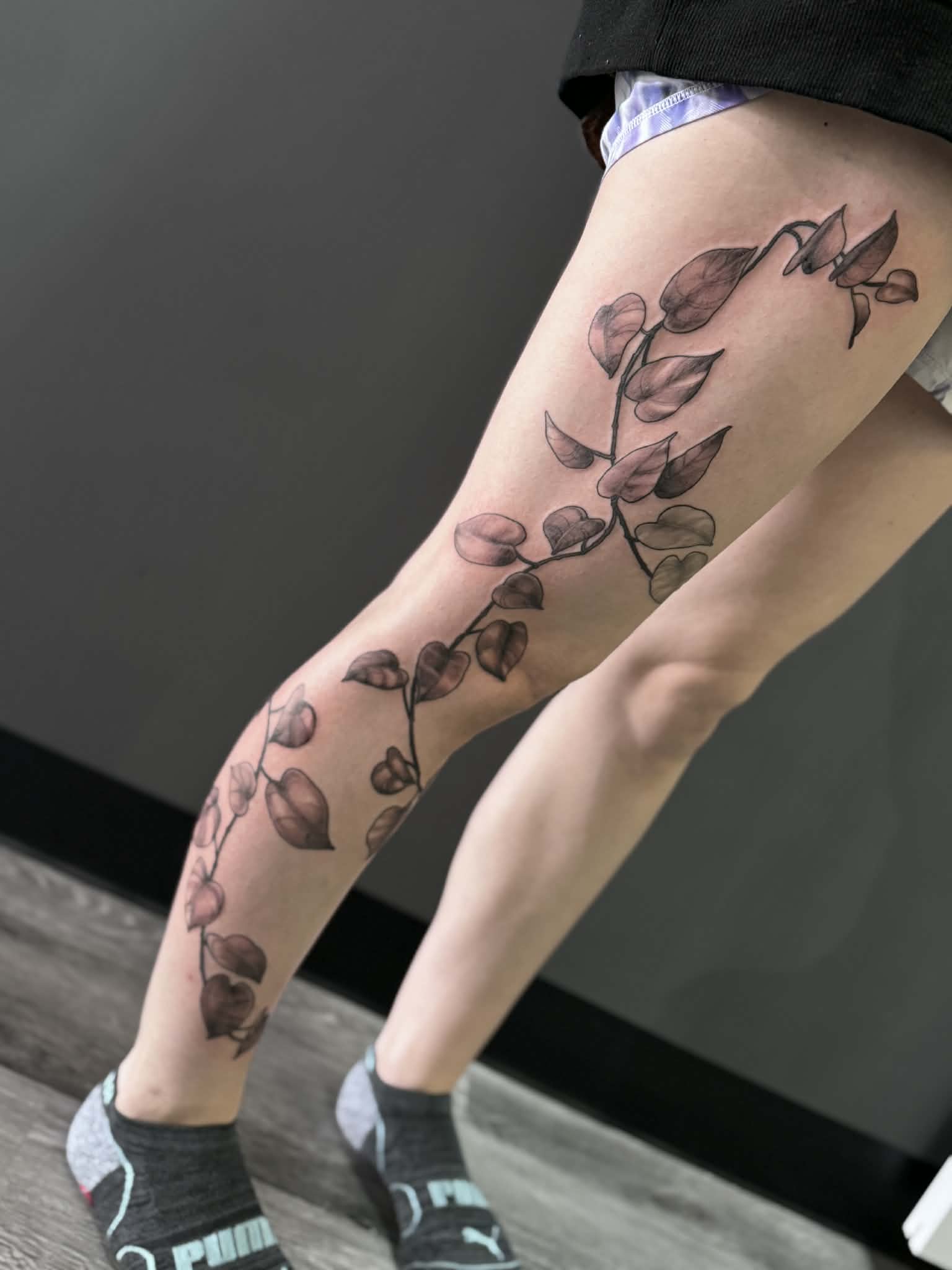 Custom black and grey illustrative vine tattoo covering the full leg, showcasing detailed leaf shading by AJ at Poking Hazard in Edmonton, AB