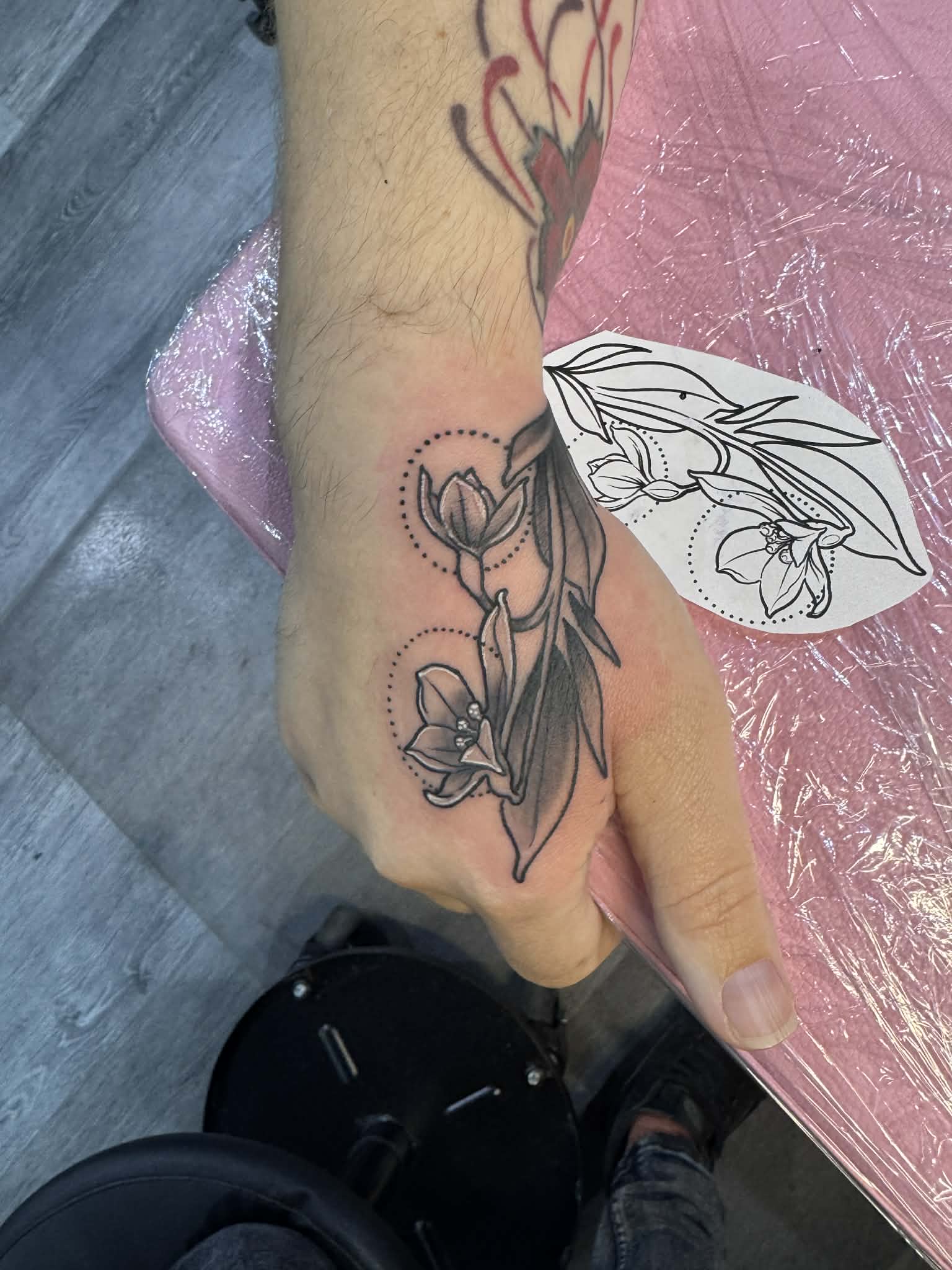 Custom illustrative lily hand tattoo with geometric dot-work accents, showcasing precise stencil-to-skin execution by AJ at Poking Hazard’s private studio in Edmonton, AB.