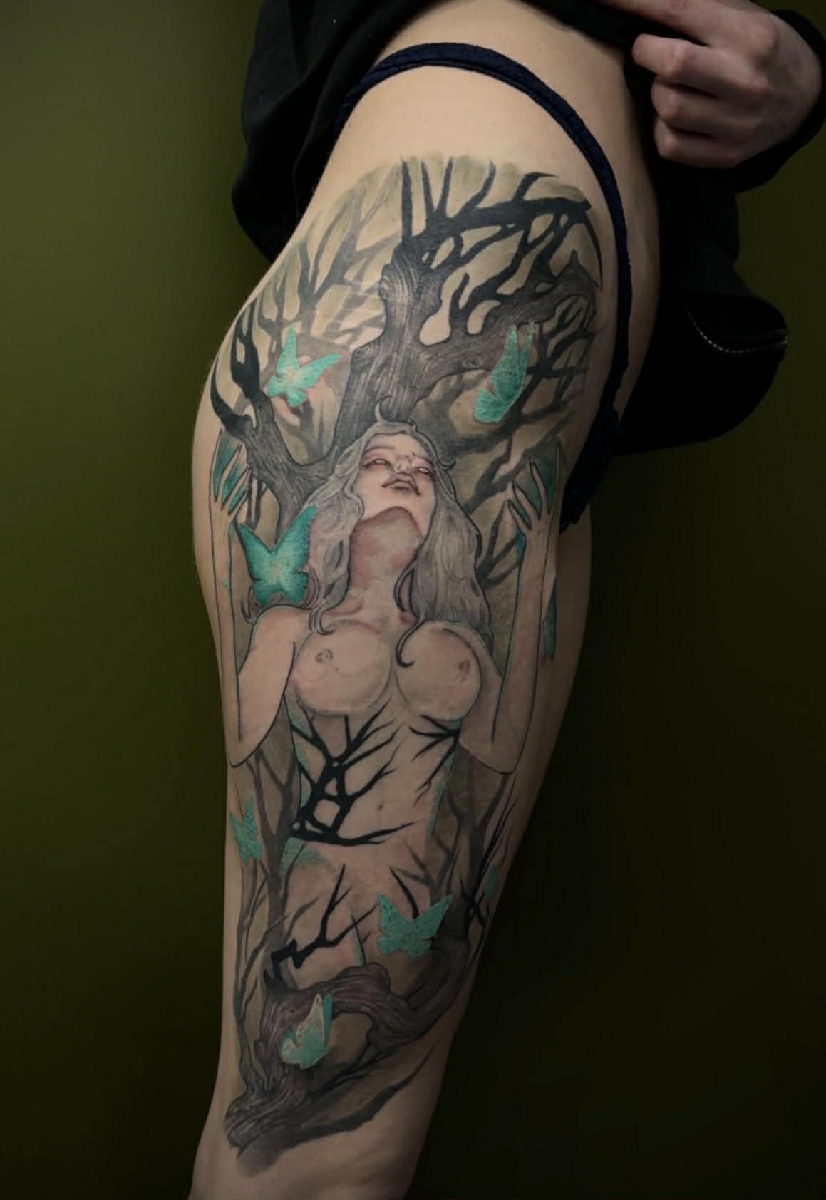 Large illustrative hip tattoo of a woman merging with a tree, featuring glowing teal butterflies and detailed shading, by AJ at Poking Hazard’s private skin-informed studio in Edmonton, AB.