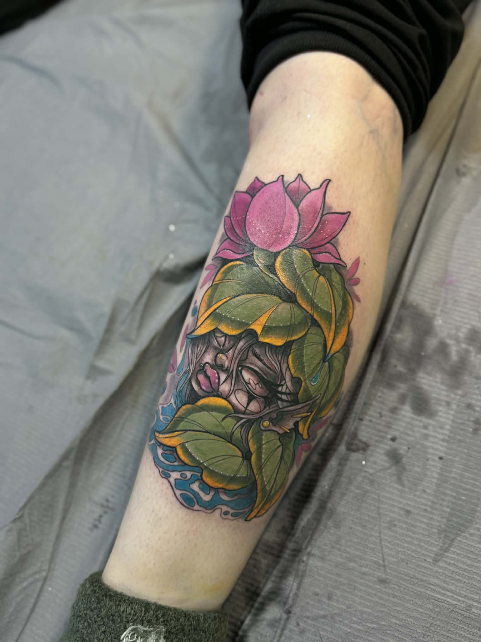 Vibrant neo-traditional leg tattoo featuring a pink lotus with a hidden woman's face integrated into the leaves, demonstrating expert color saturation by AJ at Poking Hazard in Edmonton, AB.