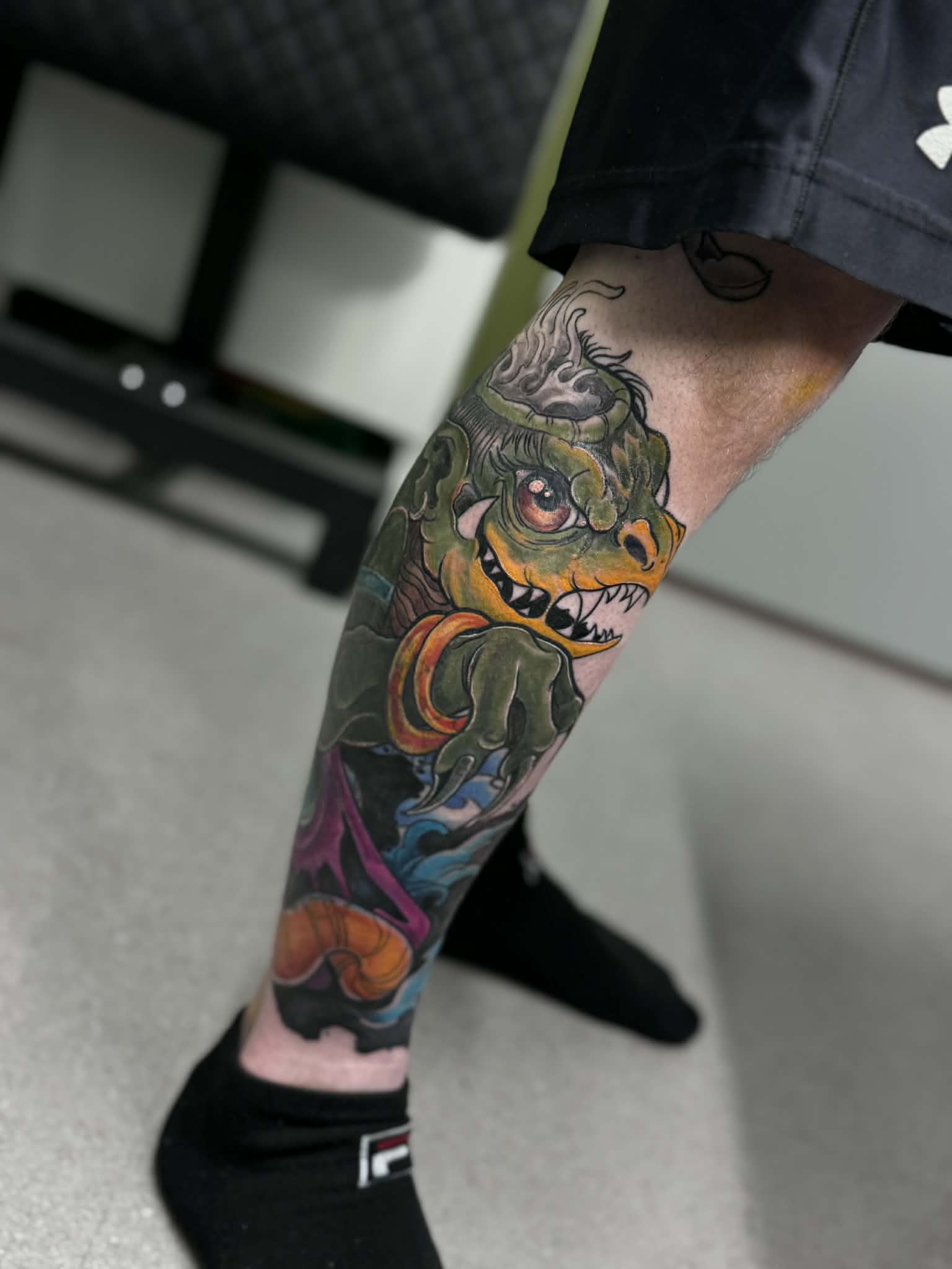 Vibrant neo-traditional leg tattoo of a green monster character with bold saturation and flowing water details, by AJ at Poking Hazard’s private skin-informed studio in Edmonton, AB.